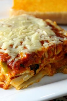 a white plate topped with lasagna next to a slice of bread on top of a table