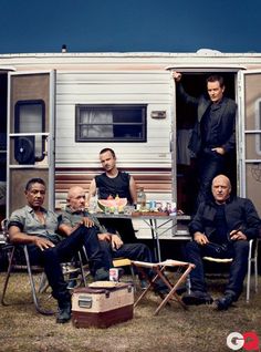 four men are sitting in chairs outside an rv with food and drinks on the table