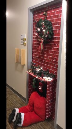 an elf is laying on the floor in front of a brick wall and christmas wreath