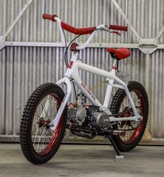 a white bicycle with red rims parked in front of a metal fence and building