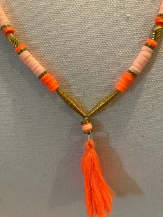 an orange and white necklace with tassels hanging from it's end on a wall