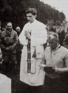 a black and white photo of a man in a priest's outfit with other people around him