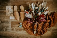 an arrangement of flowers, shoes and pictures on a wooden floor next to a scarf