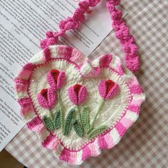 a crocheted heart shaped purse sitting on top of a table next to an open book