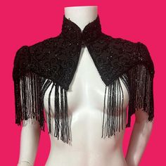 A late 19th century capelet made from silk grosgrain. This has a collared neck and hook and eye fastenings at the front.  The elongated v cut hem is finished with a beaded fringe and there is beading over the capelet itself.  There are some missing strands of beading, but not enough to be overly conspicuous. There are also a few hanging threads that remain where there should be beads.  There is some shred around the neck and on the shoulders.  The beaded design is mostly intact, but there are a Fitted Evening Shawl, Elegant Fitted Cape For Costume Party, Fringed Shawl For Party, Victorian Capelet, Posture Collar, Motifs Perler, Beaded Fringe, V Cut, V Cuts