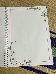 an open notebook with pink flowers and green leaves on the cover is sitting on a bamboo mat