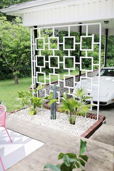 a white car is parked in front of a house with plants on the lawn and an outdoor seating area