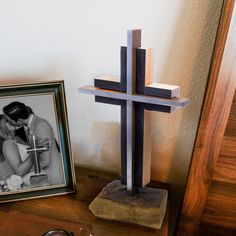 a wooden cross sitting on top of a table next to a framed photo and eyeglasses