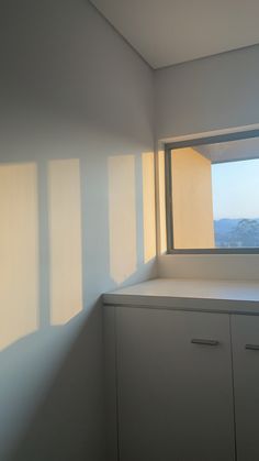 an empty room with the sun shining through the window and on the wall, there is a cabinet that has drawers in front of it