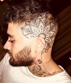 a man with a flower tattoo on his head and behind him is a white t - shirt