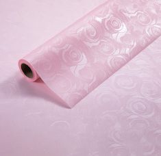 a roll of pink tissue paper sitting on top of a white tablecloth covered in swirls