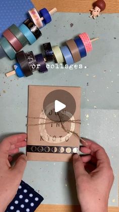 someone is holding up a box with some tape on it and there are several spools of thread in the background