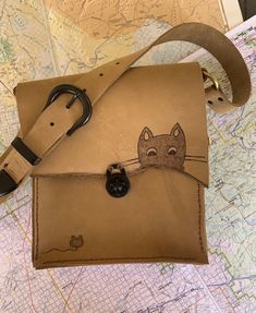 Adorable Cat and mouse on light brown leather purse. This bag is 9x8 with a 16 inch strap. The Phone pouch and the card pocket are plaid print on leather.  My bags are inspired by the Swiss Army Knife, made to last a lifetime with useful features. I like distressed leather and rugged edges. I feel it gives my pieces their own personality. All items are 100% made by me, from design to all the hand sewing (saddle stitch) .Each bag takes about 8 hours of work time. Cat Design Crossbody Shoulder Bag For Everyday Use, Everyday Use Crossbody Shoulder Bag With Cat Design, Everyday Crossbody Shoulder Bag With Cat Design, Cat Design Pouch Shoulder Bag For Travel, Travel Pouch Shoulder Bag With Cat Design, Travel Shoulder Bag With Cat Design, Cat Design Shoulder Satchel, Beige Bag With Cat Design For Everyday Use, Beige Cat Design Bag For Everyday Use