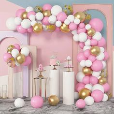 a pink and white balloon arch with gold balloons on the top, along with other decorations