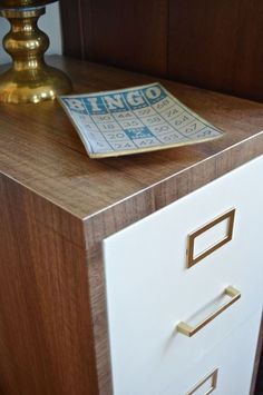 a close up of a drawer with a magazine on it's top and a lamp in the background