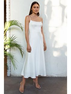 a woman wearing a white dress standing in front of a plant