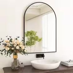 a white sink sitting under a mirror next to a vase with flowers