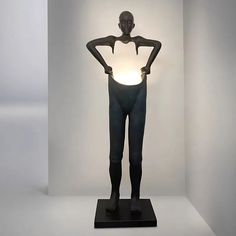 a black mannequin standing in front of a white wall with a light on it's back