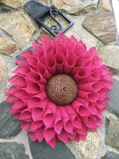 a large pink flower sitting on top of a stone wall next to a metal hook