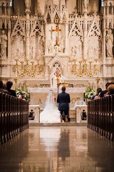 a bride and groom standing at the alter in front of an ornate church with pews