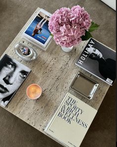 a coffee table topped with books and flowers next to a vase filled with pink hydrangeas