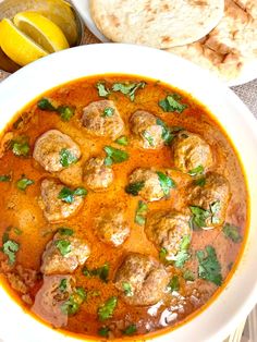 a white bowl filled with meatballs and sauce next to pita bread on a table