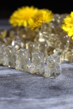 small clear bears sitting next to yellow flowers on a gray surface with black background and white border