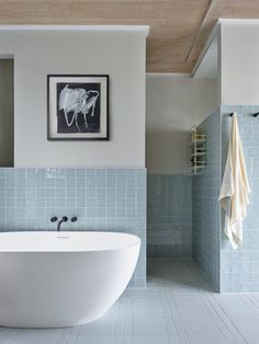 a white bath tub sitting next to a blue tiled wall in front of a painting