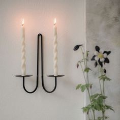 two candles are hanging on the wall next to a vase with flowers