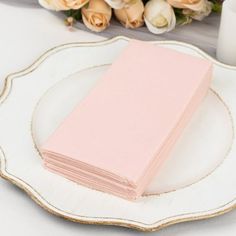 a pink napkin sitting on top of a white plate next to a bouquet of roses