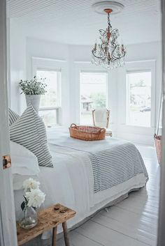 a white bedroom with a chandelier hanging from the ceiling and pillows on the bed