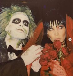 two people dressed up in costumes and makeup posing for the camera with roses around their necks