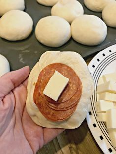 a person holding a piece of bread with cheese on it next to other food items