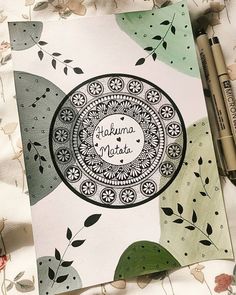 a notebook with an intricate design on the cover and some markers next to it in front of a flowery background