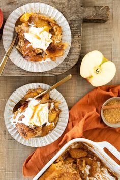 two plates filled with apple cobbler next to an orange towel and spoons on a wooden table