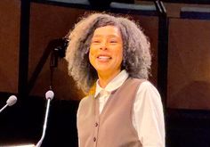 a woman standing at a podium in front of a microphone with an afro on her head