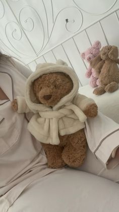 a woman laying in bed with her teddy bear wearing a robe and hoodie on