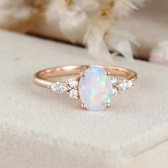 a white opal and diamond ring sitting on top of a piece of cloth with flowers in the background