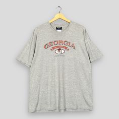 a grey t - shirt hanging on a hanger with the word georgia in red