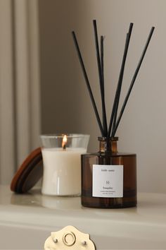 a candle and some candles sitting on a table next to a glass container with reeds in it