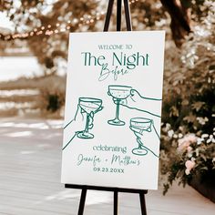 a welcome sign for the night before dinner is displayed on an easel in front of some flowers