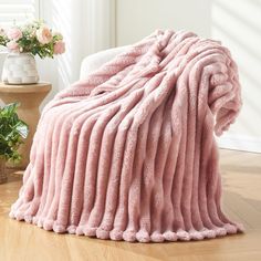 a pink blanket sitting on top of a wooden floor next to a potted plant