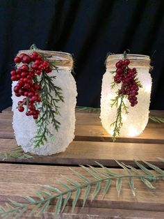 two mason jars decorated with red berries and greenery are sitting on a wooden table