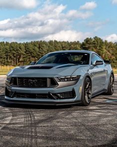 the front end of a silver mustang on a race track with trees in the background