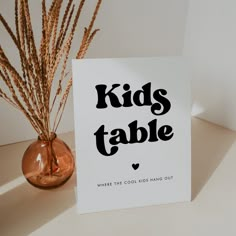 there is a card that says kids table next to a vase with dry grass in it