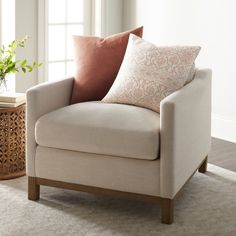 a chair with two pillows on it next to a table and potted plant in the corner