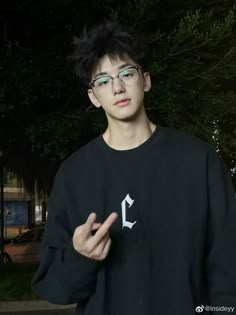 a young man wearing glasses standing in front of a tree with his hand up to the camera