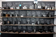 a blackboard with writing on it and various cameras sitting on shelves in front of the wall