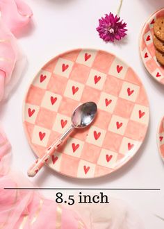 a pink plate with hearts on it next to two cookies and a spoon that says 8 5 inch