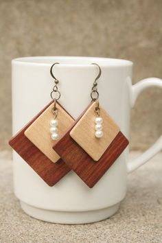 a pair of wooden earrings with pearls hanging from it's earwires on a white cup